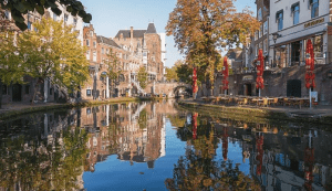 A picture of a canal in the Dutch city of Utrecht during autumn, showing the beauty of the historic buildings and waterside cafes, which reflects the charm Netherlands