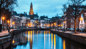 A picture of a canal in the city of Groningen at dusk, where the lights illuminate the historic buildings, reflecting the charm Netherlands.