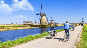A picture of people cycling near windmills and a canal, a famous experience 
