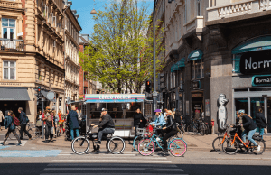 A picture of a busy city street with many bicycles, featuring local food vendors and traditional buildings, reflecting the vibrant atmosphere of a European capital.