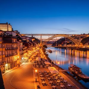 Evening view of Porto along the Douro River, showing illuminated historic buildings, cobbled streets, charming bridges, and riverside cafes. Scenic reflections in the water, highlighting the city’s romantic atmosphere, authentic architecture, and less-crowded, tranquil vibe. Realistic travel photography, warm lighting, no people present, emphasizing cultural depth and scenic beauty.